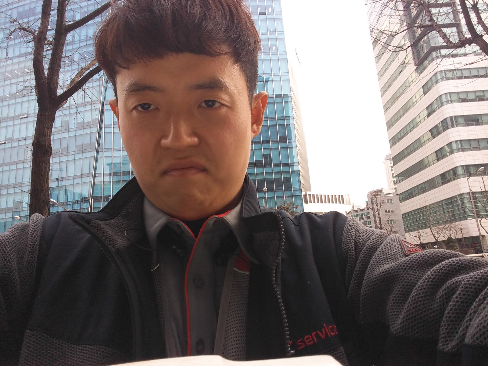 고층 빌딩 사이에서 회사 점퍼를 입고 찍은 셀카