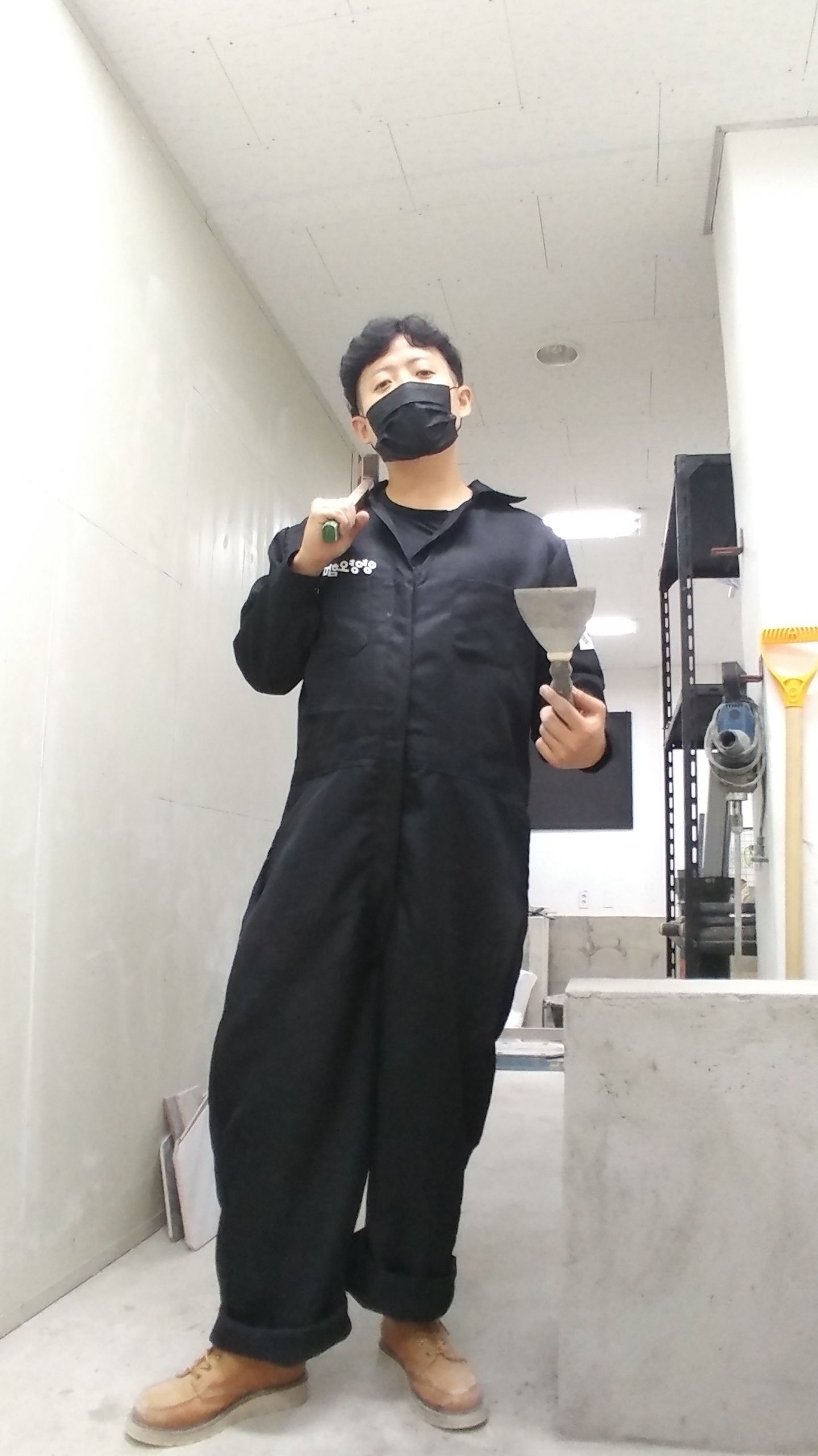 검은 작업복에 마스크를 쓰고 미장 도구를 든 사진