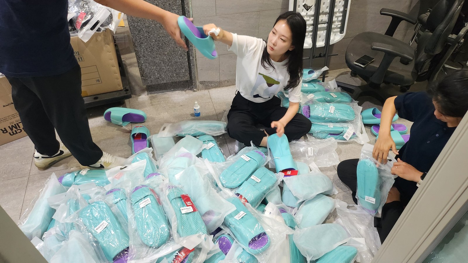 바닥에 가득 펼친 슬리퍼 상품을 여럿이 살펴보는 모습