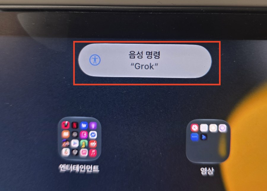 아이패드 홈 화면 위쪽에 음성 명령, Grok 이라고 적힌 말풍선이 떠 있고 빨간 상자로 표시돼 있다.